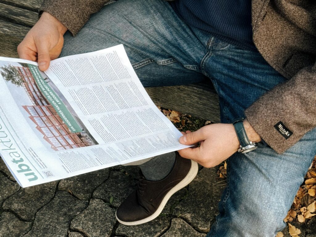 Casually dressed man reading a newspaper outdoors on a park bench in Bayreuth, Germany.